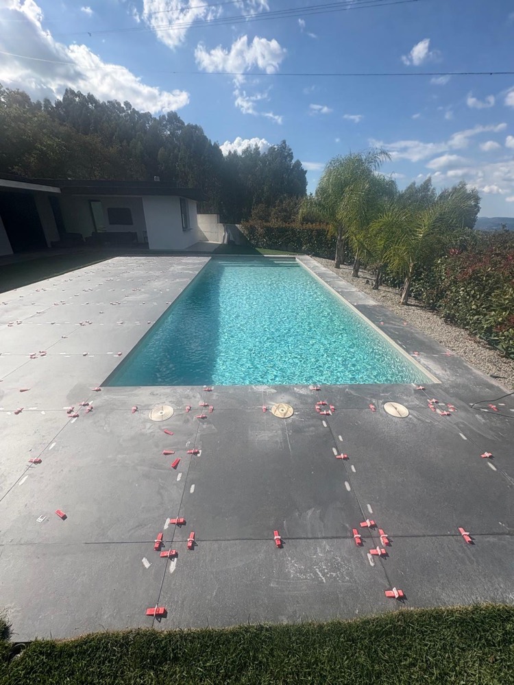 Pavimento à volta da piscina em placas cinzentas de grande formato a ser assente com niveladores