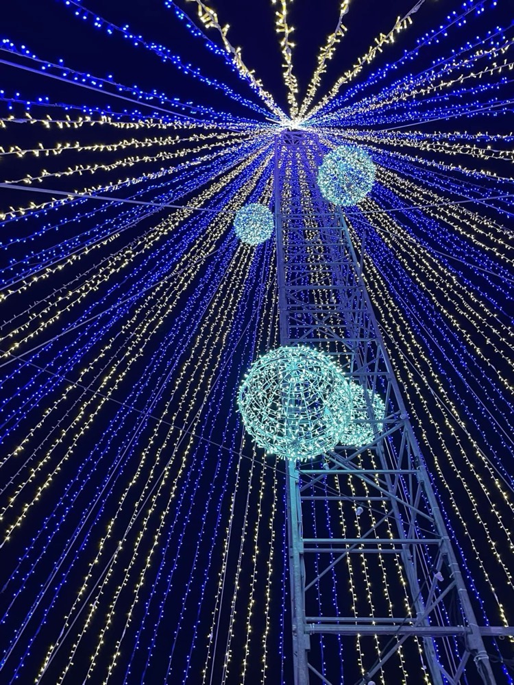 Árvore de Natal gigante feita de cordões de luz azul e branca, vista de dentro, com esferas luminosas