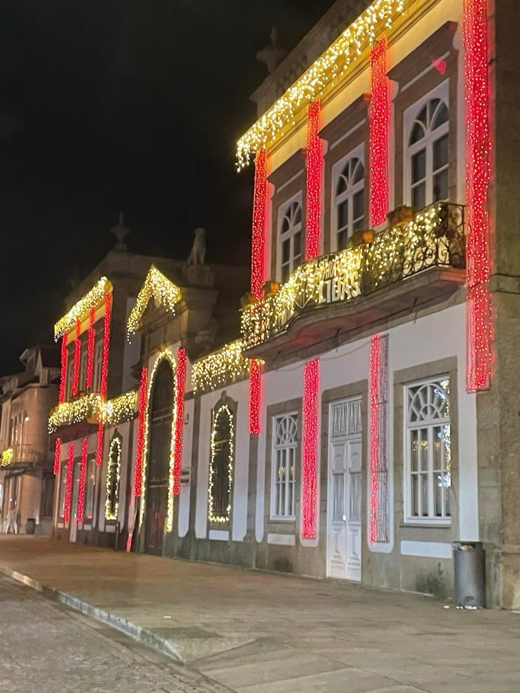 Fachada de edifício histórico decorada com cortinas de luz vermelha e franjas de luz dourada