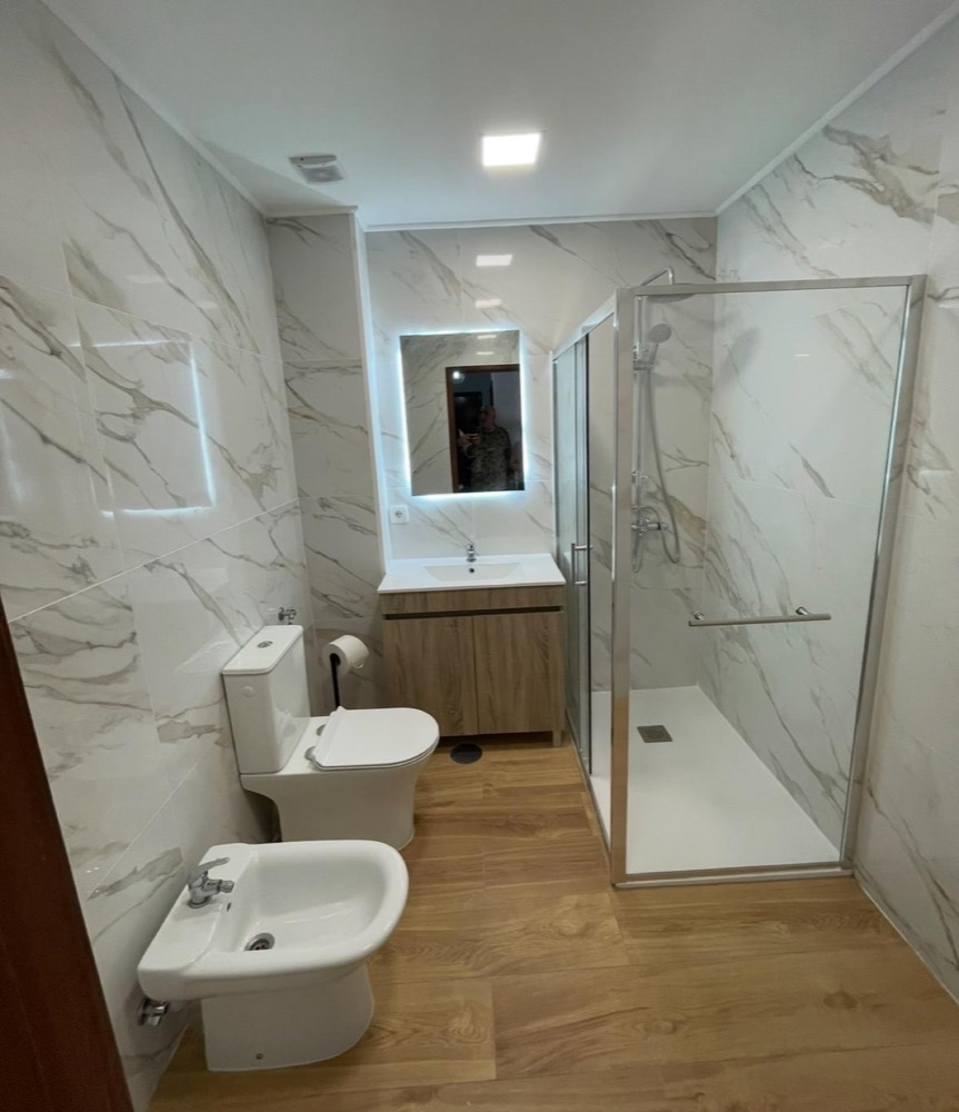 Casa de banho em cerâmica imitação de mármore com pavimento imitação de madeira, sanita, bidé, espelho com luz LED e base de duche com resguardo