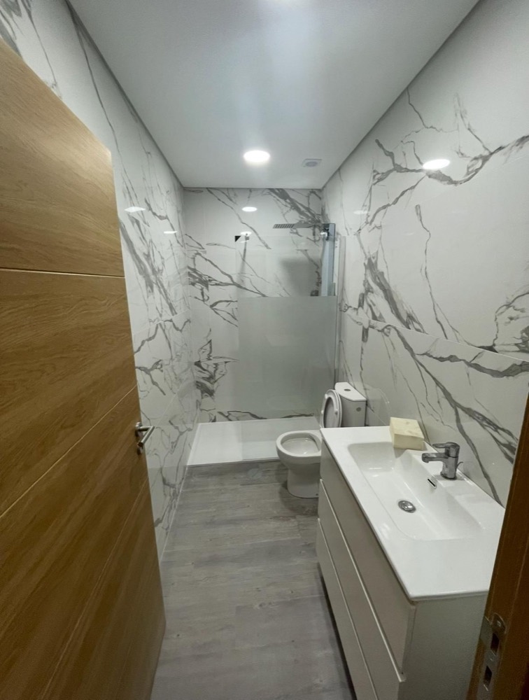 Casa de banho revestida a cerâmica imitação de mármore, com base de duche e resguardo em vidro fosco