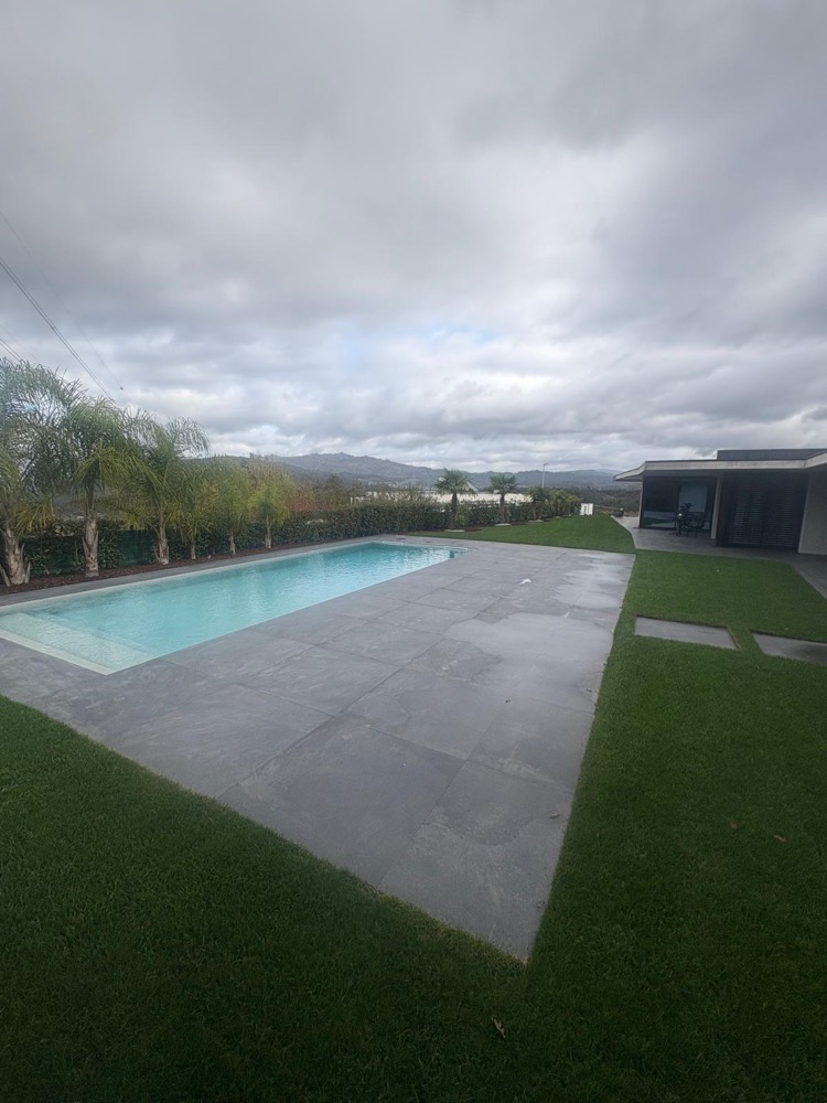 Piscina com pavimento em placas cinzentas de grande formato, relvado e palmeiras, com vista para a serra