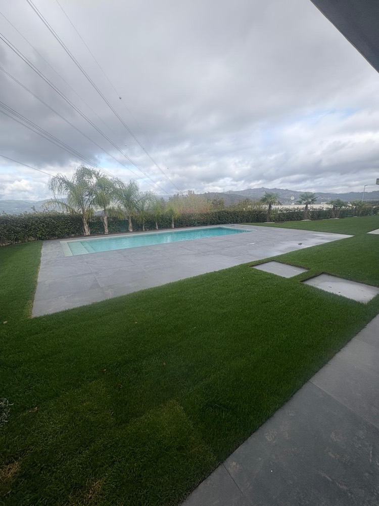 Piscina rodeada de pavimento em placas cinzentas e relvado, com caminho em placas e vista para a serra